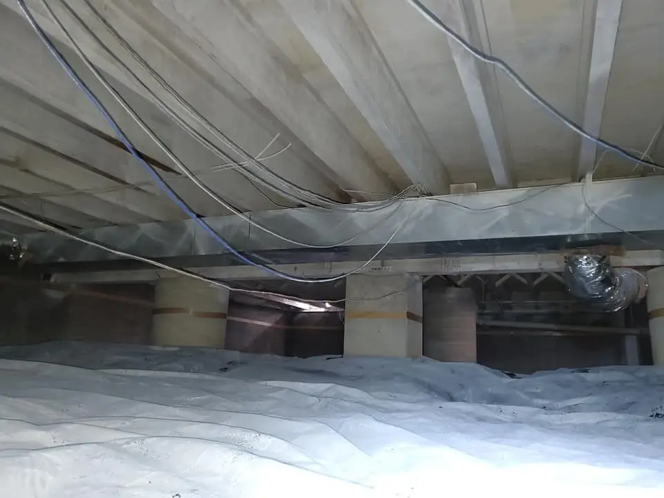 Crawlspace after encapsulation with a white vapor barrier over the floor and up the piers