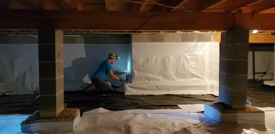 Crew member inspecting a lined crawlspace with a flashlight